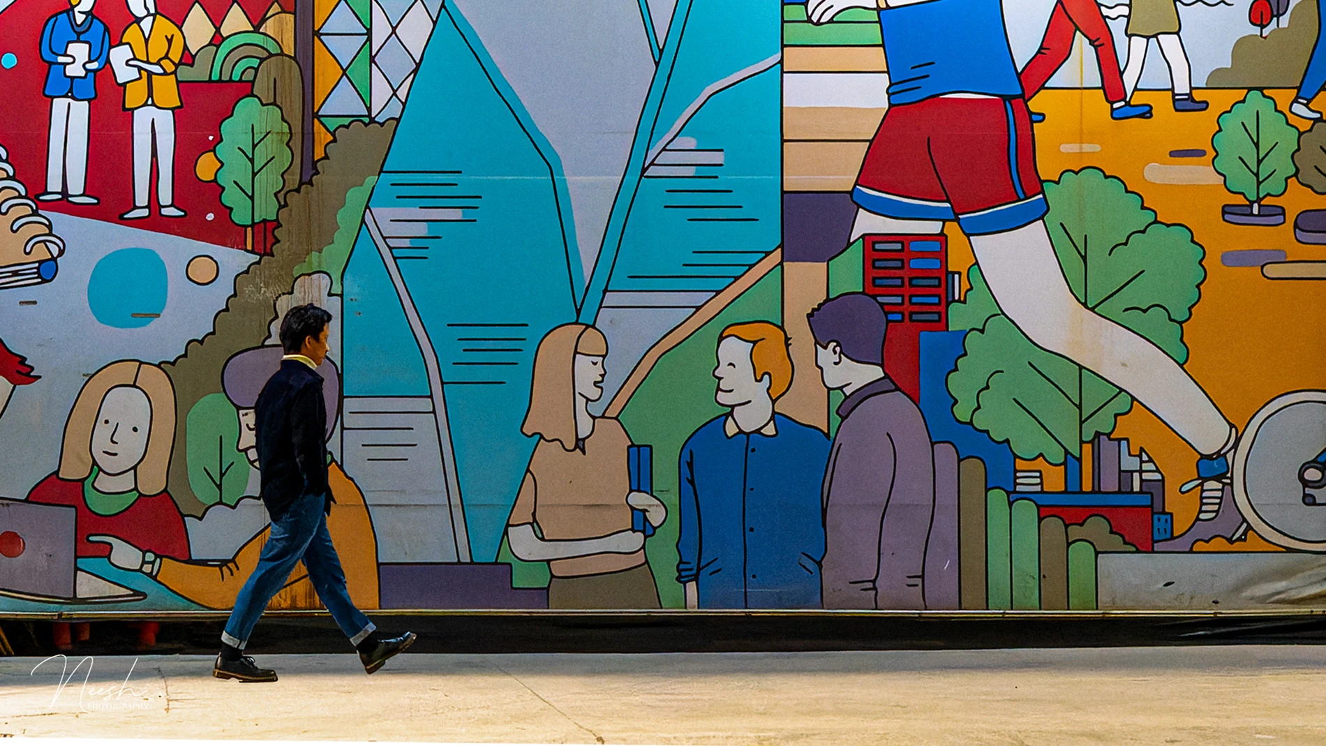 Person walking past a colorful mural of abstract figures and geometric shapes.