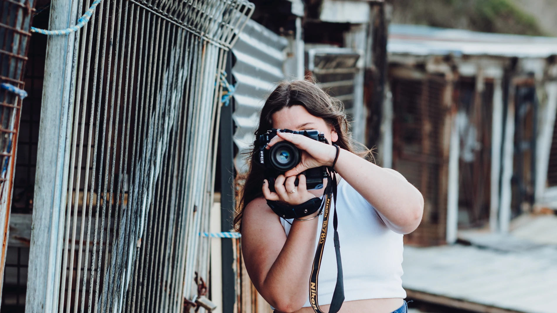 Person with Nikon camera near metal fence in rustic outdoors setting.