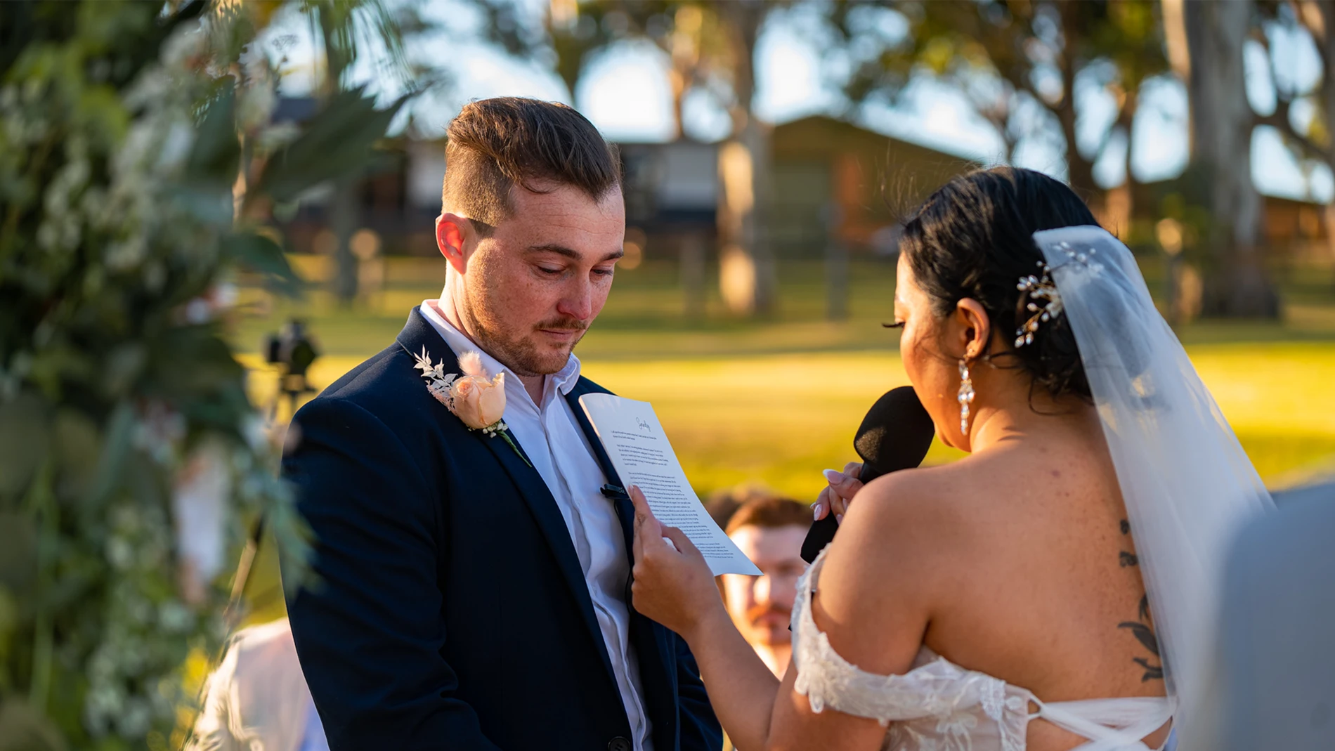 Exploring Creative Perspectives: A Glimpse Into Nick &Amp; Sandee'S Wedding Through Dual Lenses 10 Couple Exchanges Vows Outdoors On A Sunny Day With Greenery; Bride Holds Mic, Groom Listens.