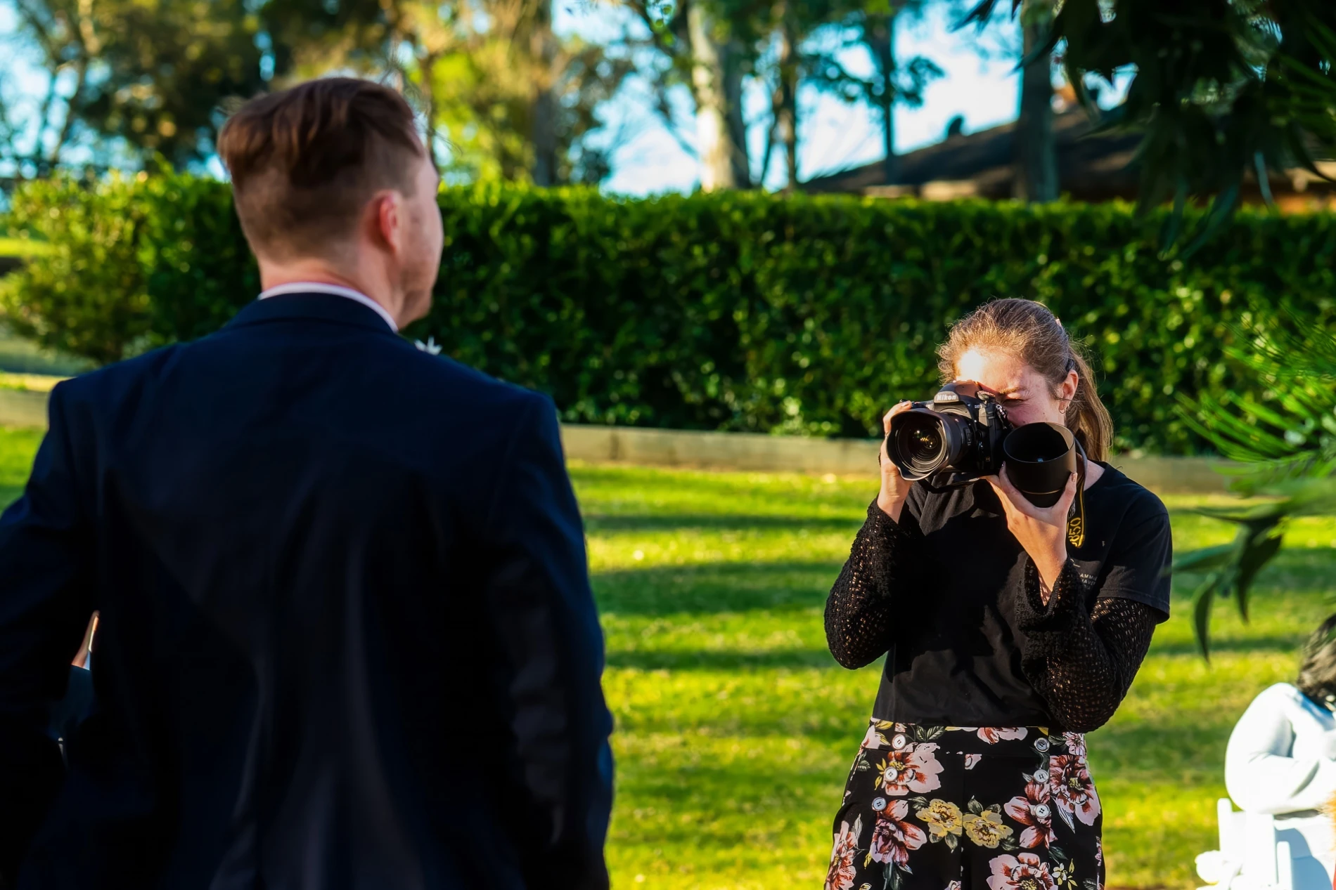 Photographer capturing a man in a suit outdoors with grass and trees in background.