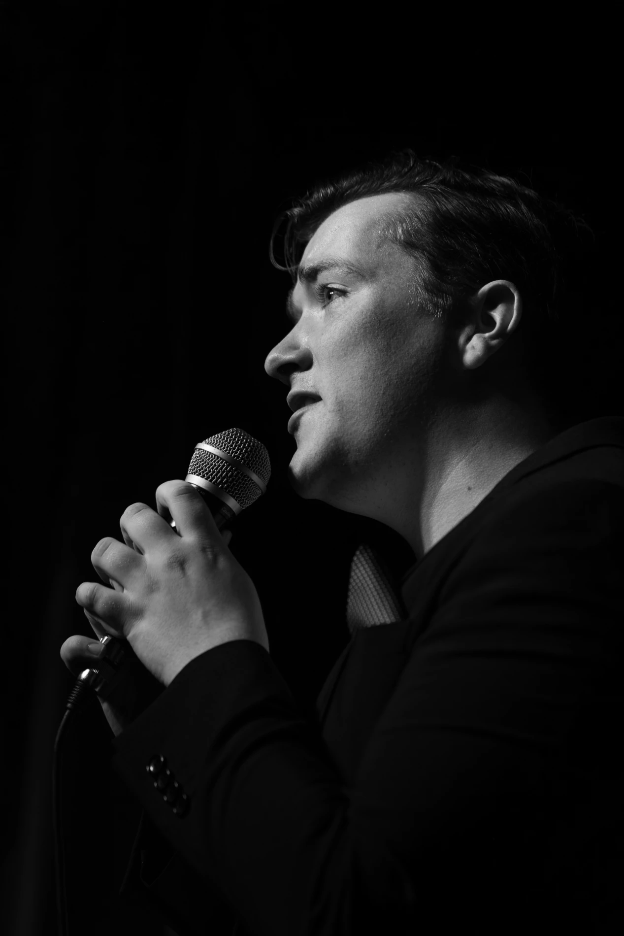 Black And White Profile Of A Person Singing With A Microphone Against A Dark Background.
