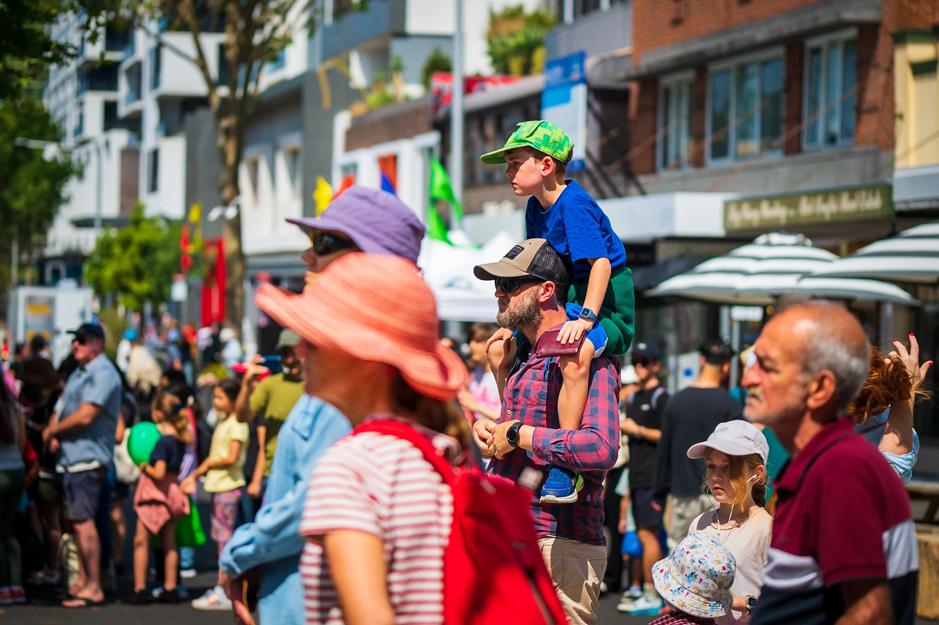 Urban Street Scene With A Crowd, Market Stalls, And A Child On Shoulders.