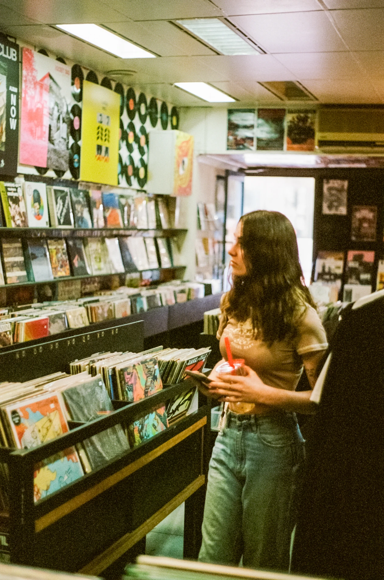 Person Browsing Vinyl Records In A Store, Holding A Drink And Smartphone.