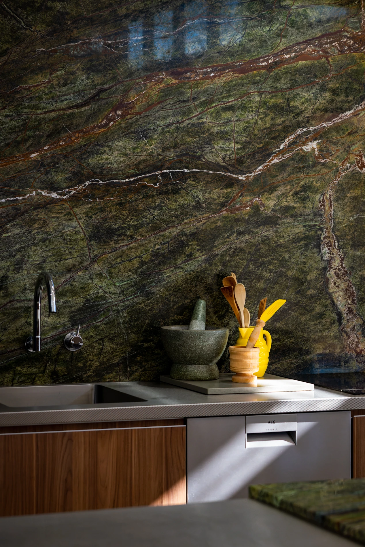 Kitchen With Green Marble Wall, Mortar And Pestle, Yellow Utensil Holder, Sink, And Dishwasher.