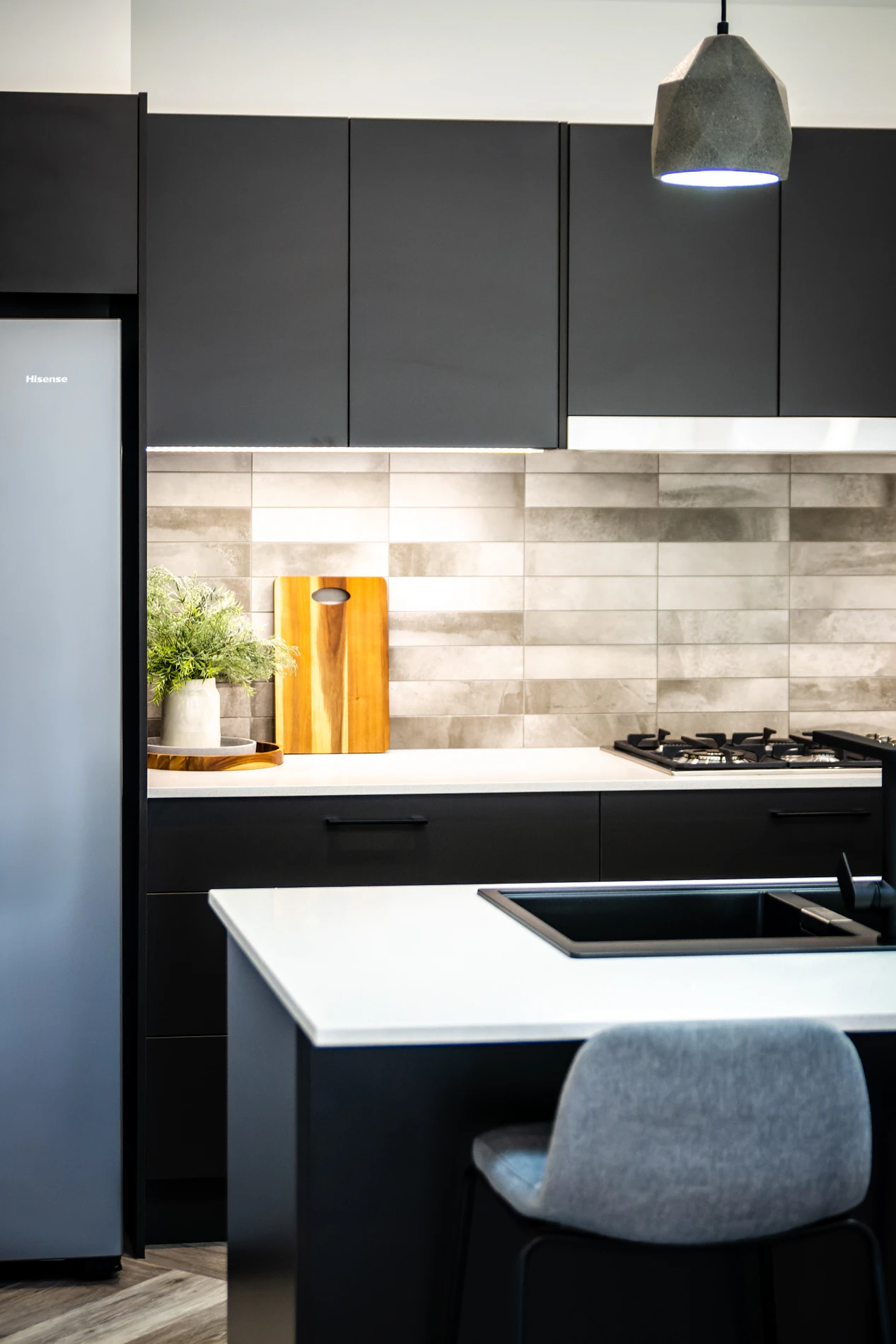 Modern Kitchen With Dark Cabinetry, Gas Cooktop, White Benchtop, And Grey Backsplash.