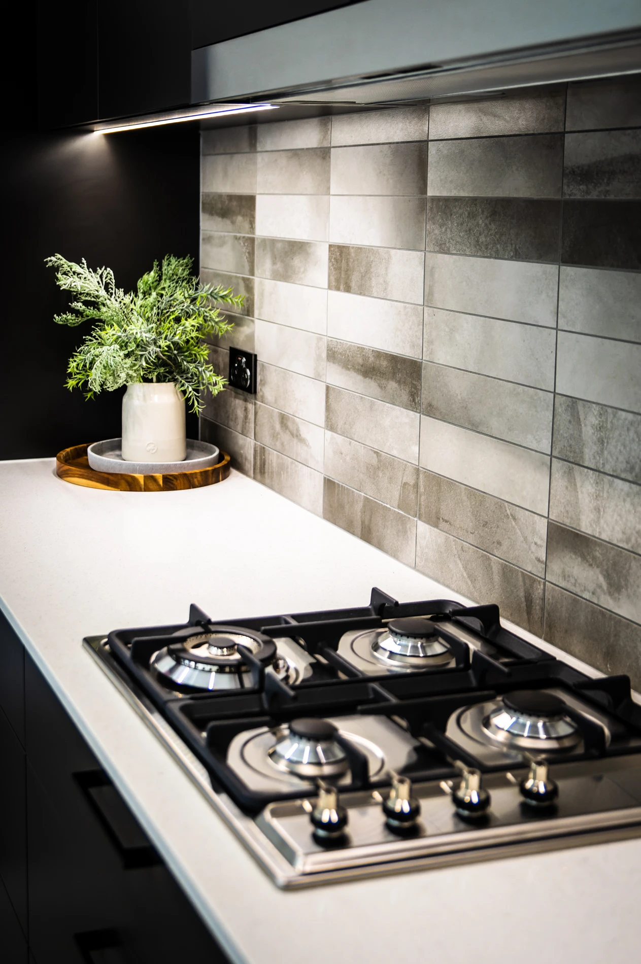 Modern Kitchen With Stainless Stovetop, Grey Tiles, And Potted Plant On White Countertop.
