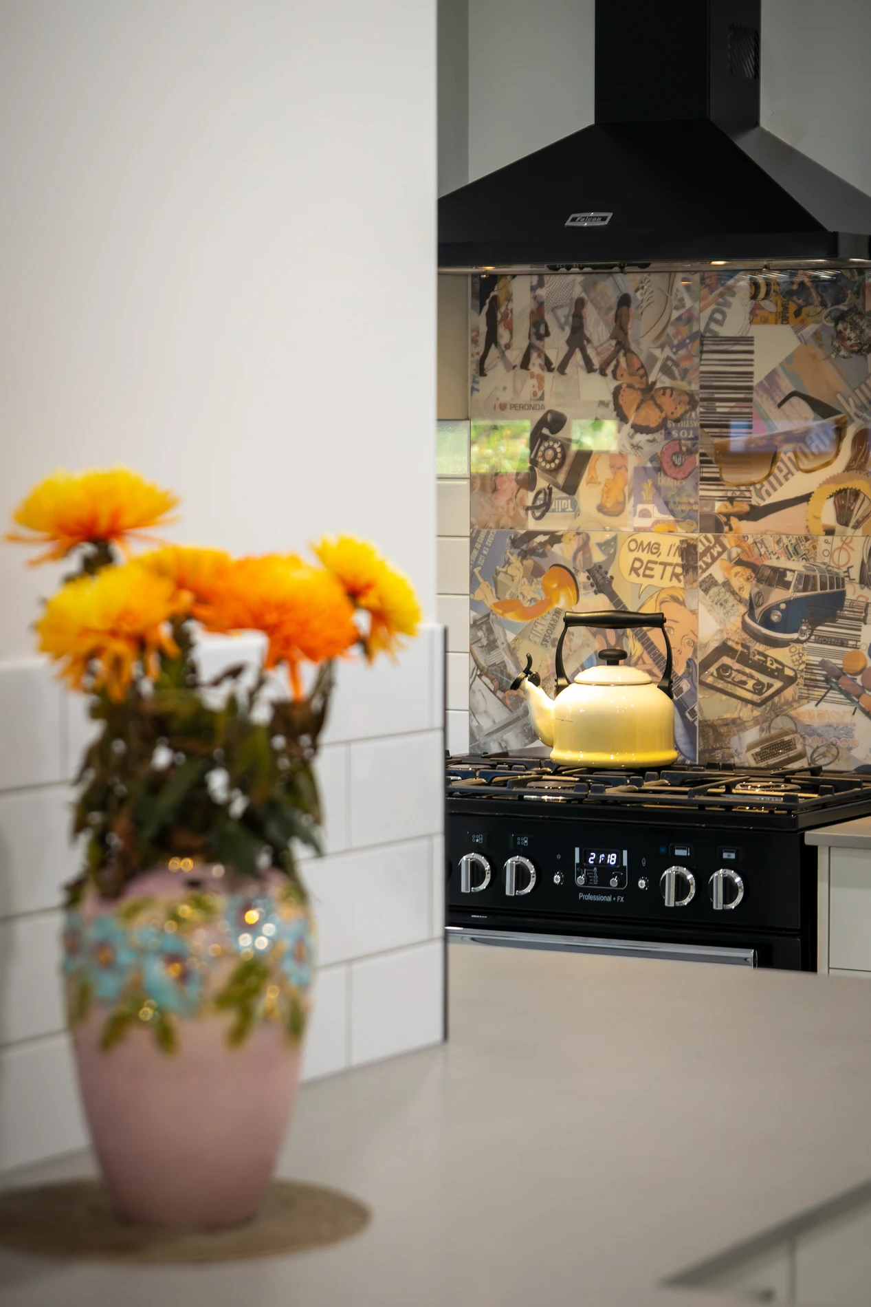 Kitchen With Yellow Flowers In A Vase, Stovetop, Oven, And Retro-Themed Backsplash.