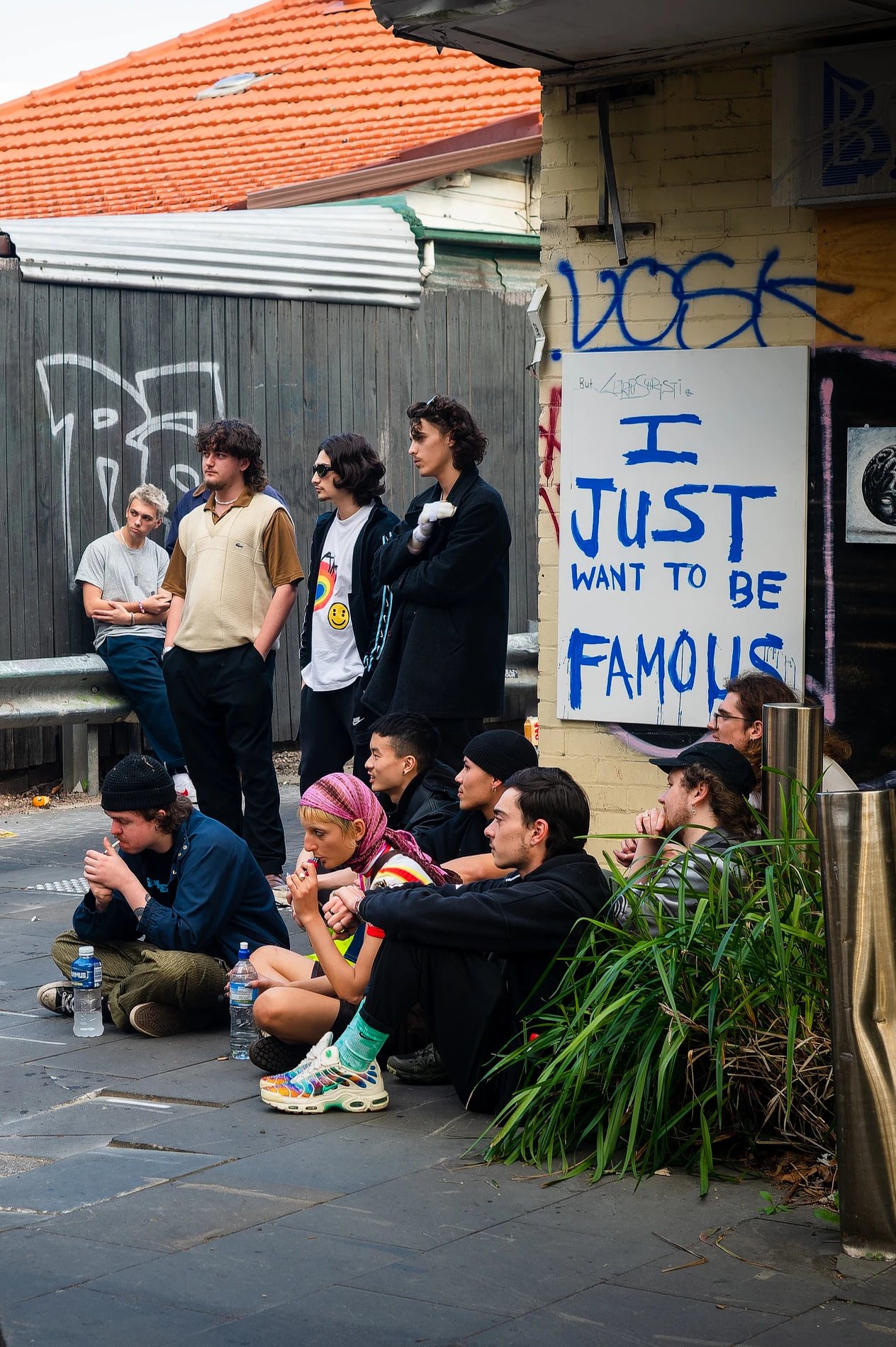 People Gathered Outdoors Near Graffiti And Poster Reading &Quot;I Just Want To Be Famous.&Quot;