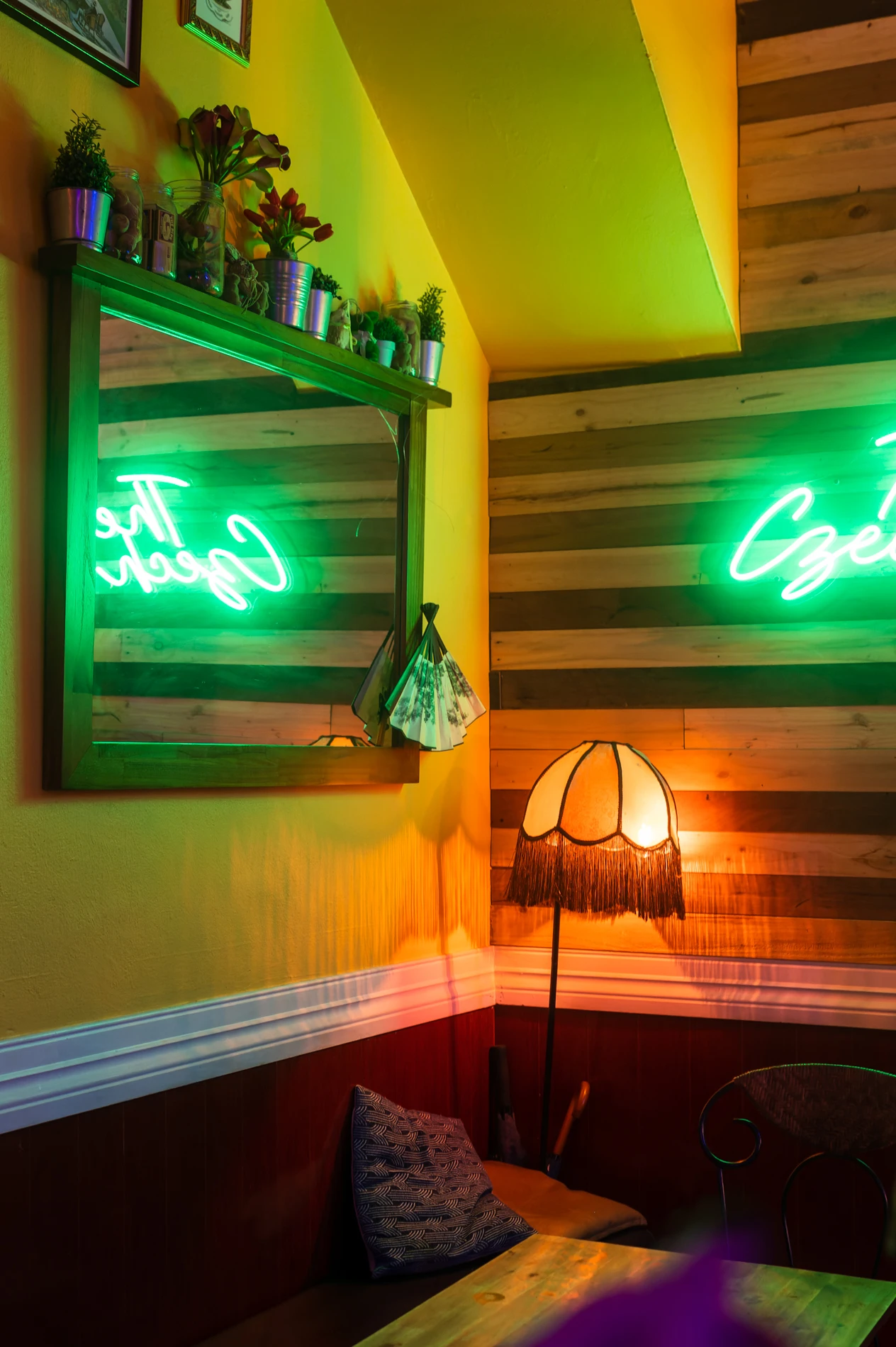 Cosy Corner With Cushioned Bench, Green Neon Sign, Mirror, Vintage Lamp, Wood Panel Walls.