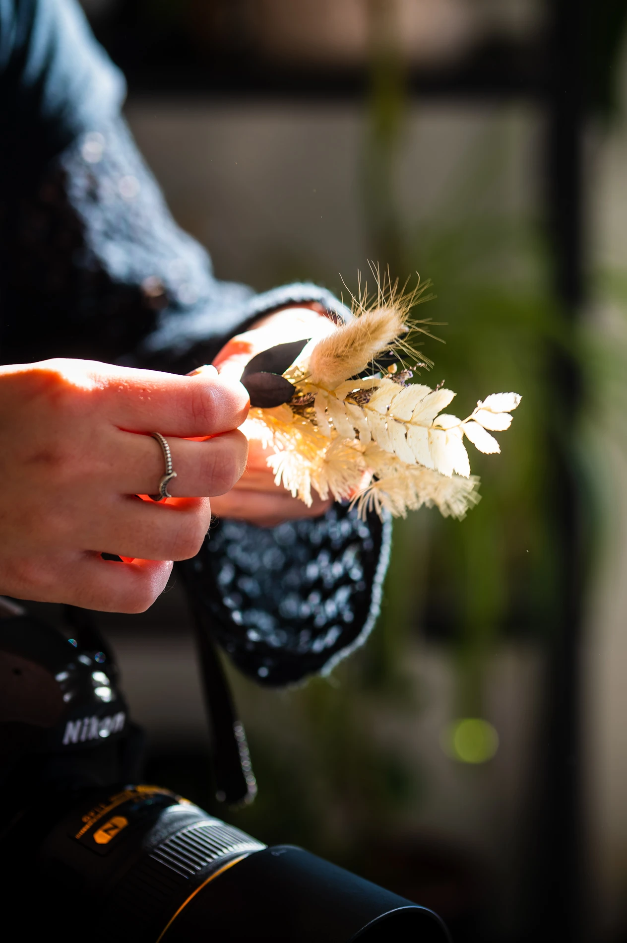 Person Holding Dried Flower Arrangement And Camera Indoors.