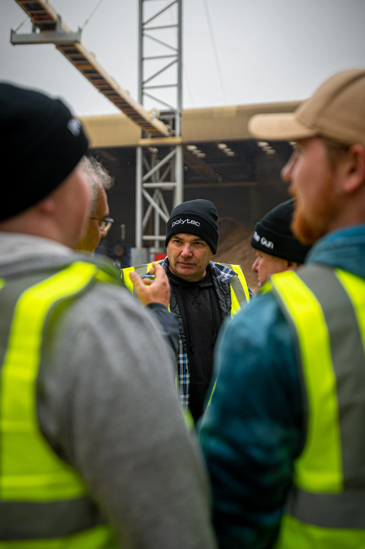 Workers In High-Visibility Vests Discuss At A Construction Site With A Crane Visible.
