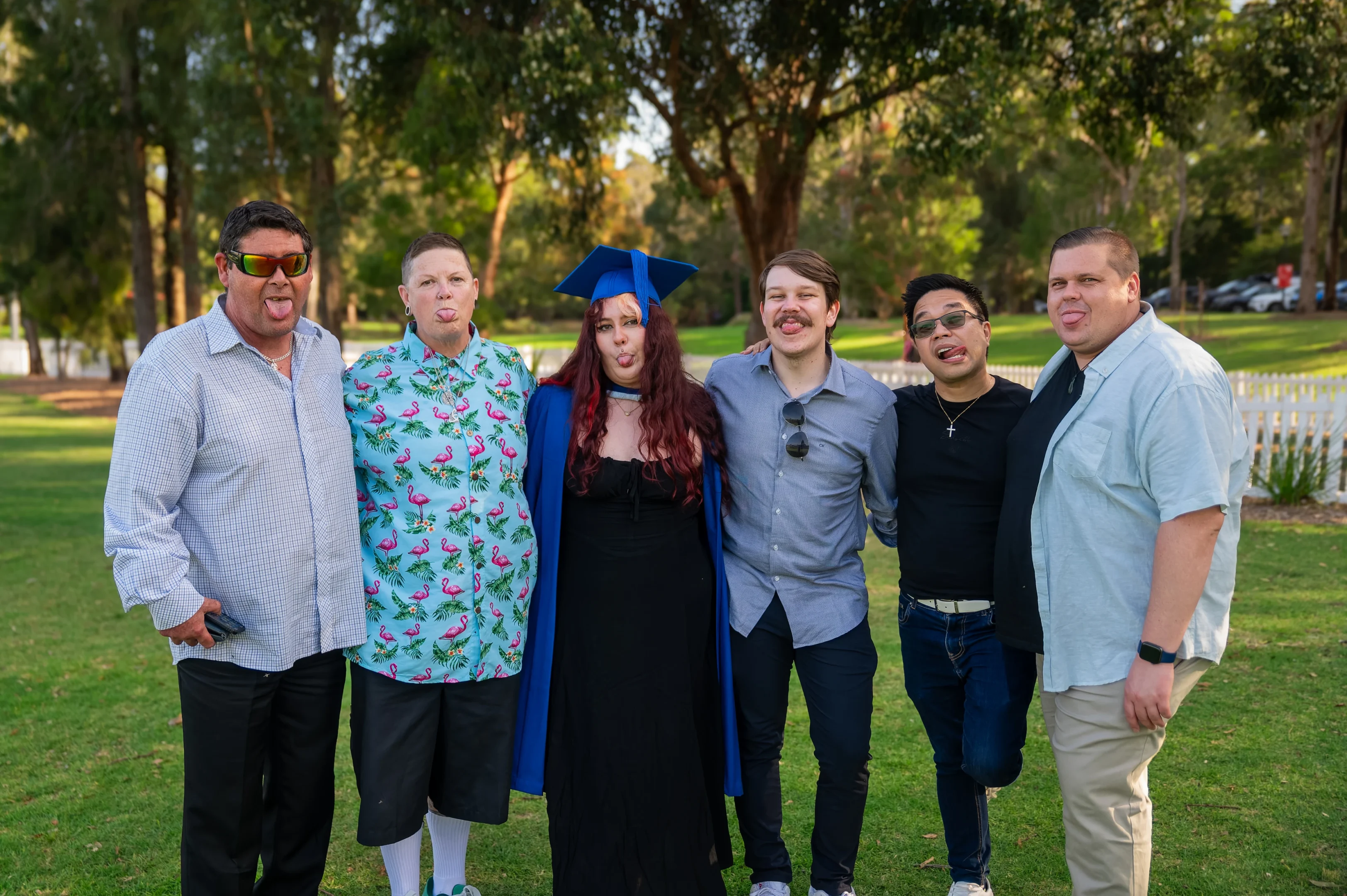 Six People Outside, Posing Playfully With Tongues Out; One In A Graduation Gown And Cap.