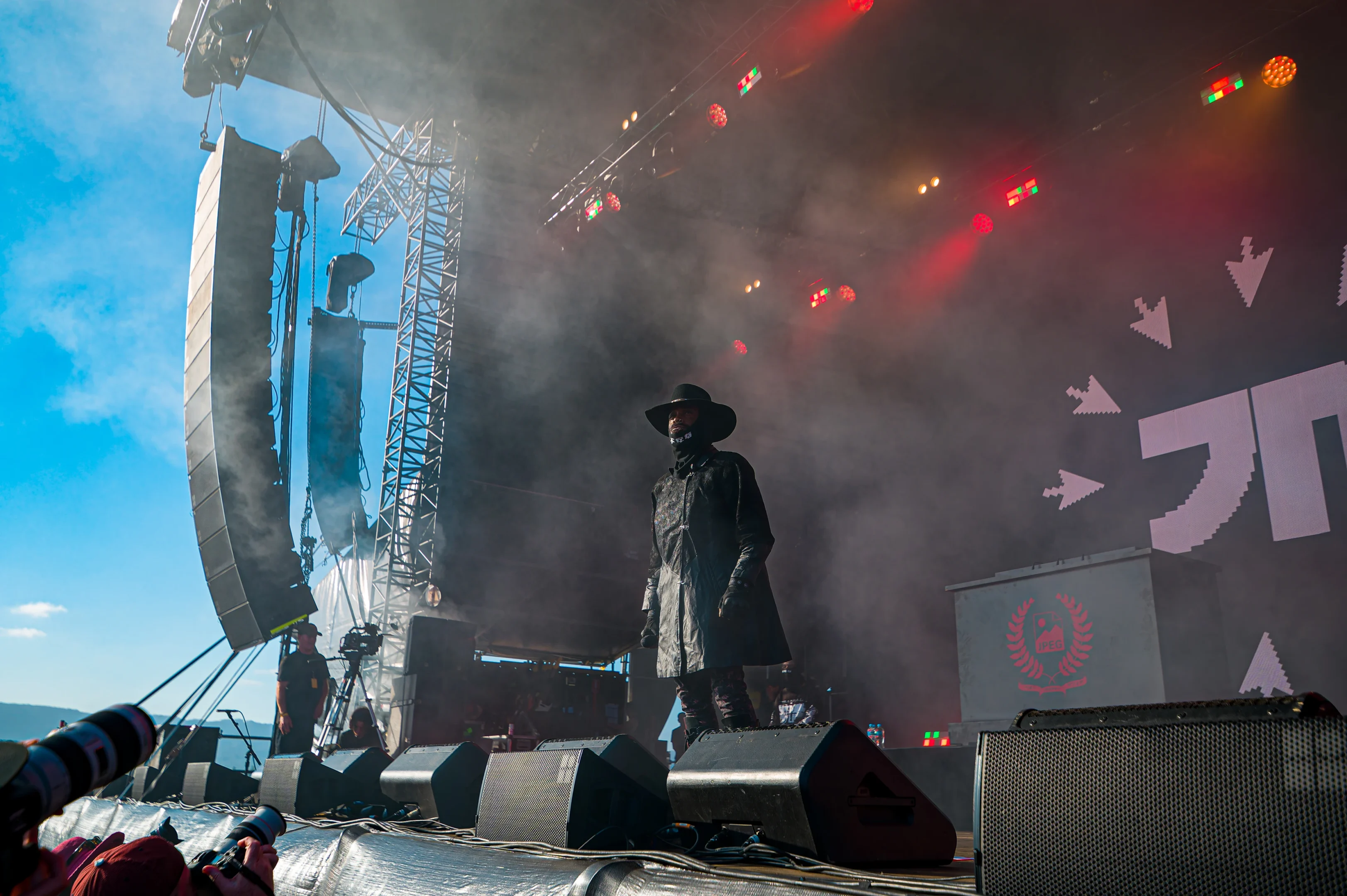 Performer In Hat On Smoky Stage With Colorful Lights, Photographers In Foreground.