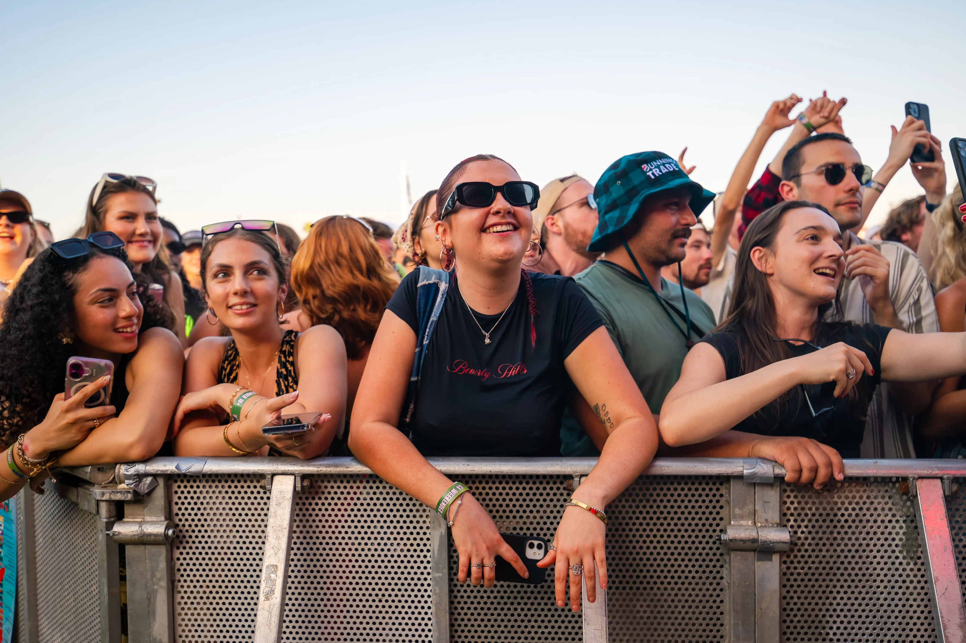 Group Of People Smiling Behind A Metal Barrier At An Outdoor Concert Event.