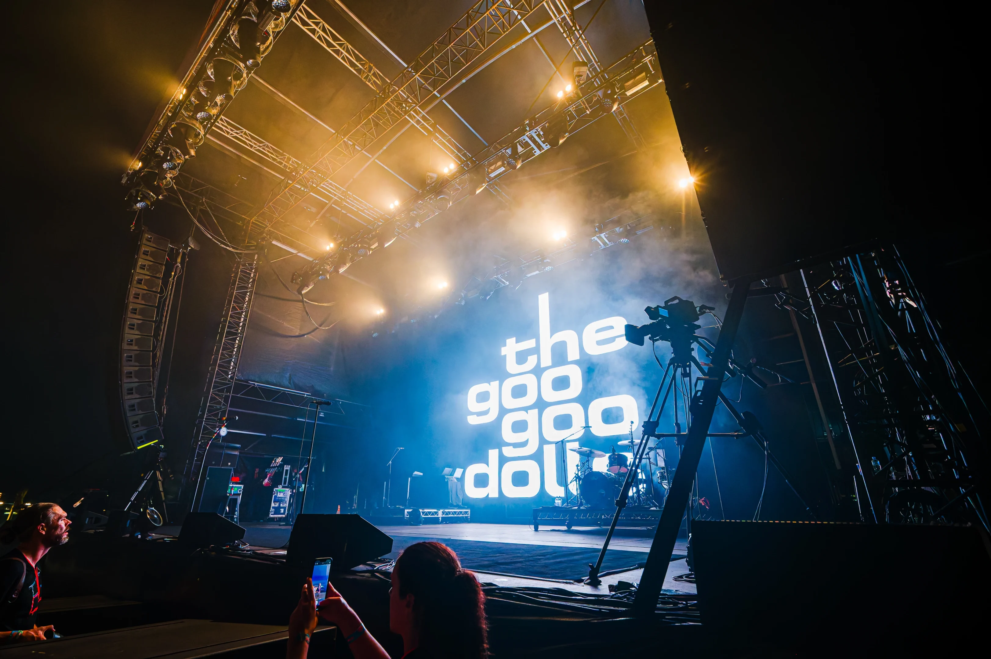 Concert Stage With Musical Equipment, Bright Lights, And &Quot;The Goo Goo Dolls&Quot; Text On Backdrop.