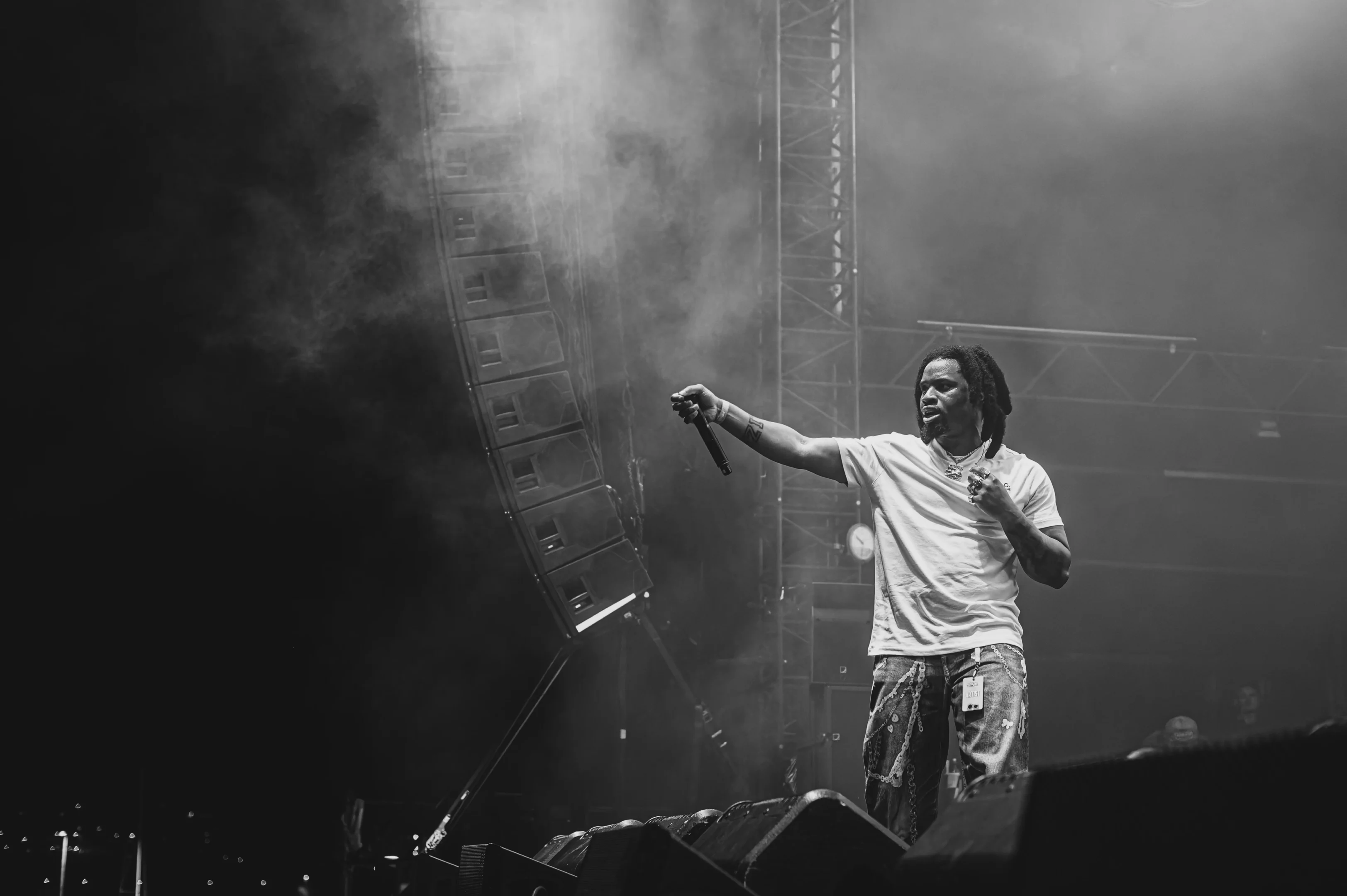 Performer On Stage With A Microphone, Gesturing, In A Foggy Concert Venue With Stage Lights.