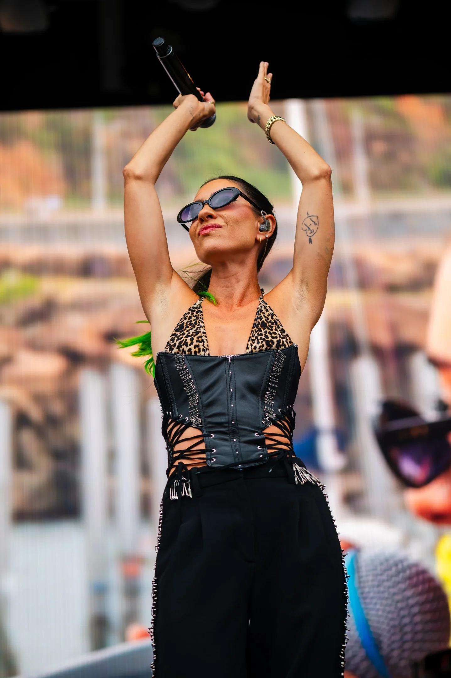 Performer On Stage With Mic, Sunglasses, Leopard Print And Leather Top, Tattoo On Left Arm.