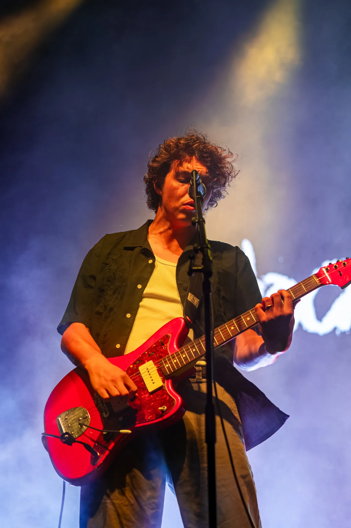 Musician On Stage With Red Electric Guitar, Dark Shirt, Light Top, Dramatic Lighting.